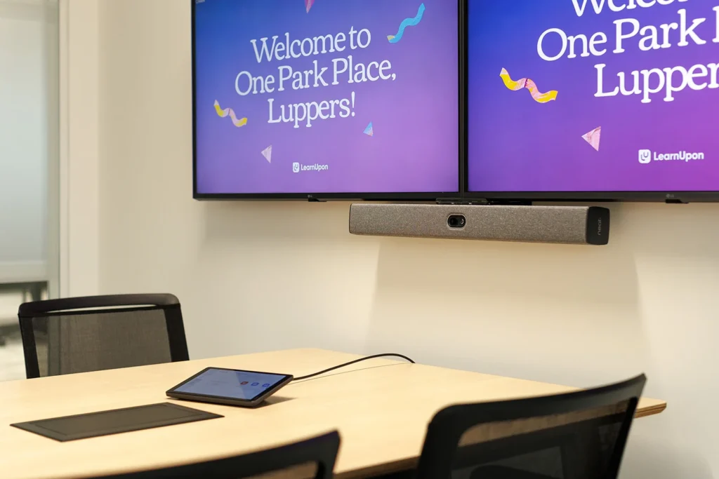 A dual screen on the wall, set up with camera, speaker, and interactive tablet in a meeting room