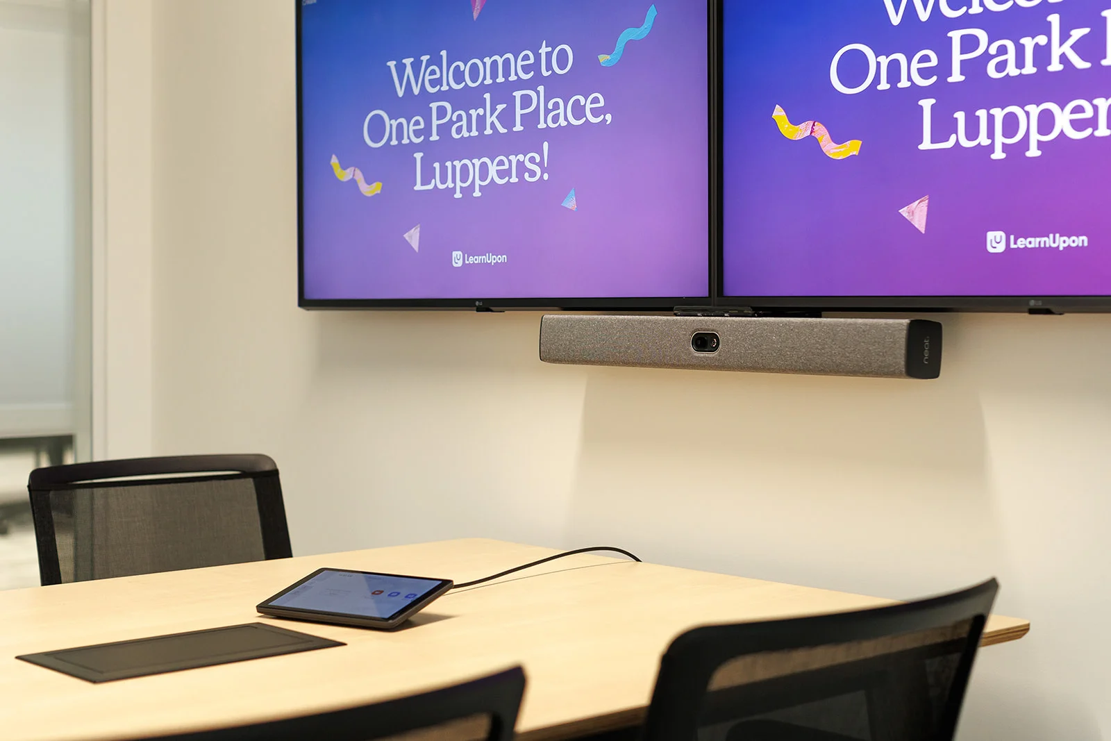 A dual screen on the wall, set up with camera, speaker, and interactive tablet in a meeting room